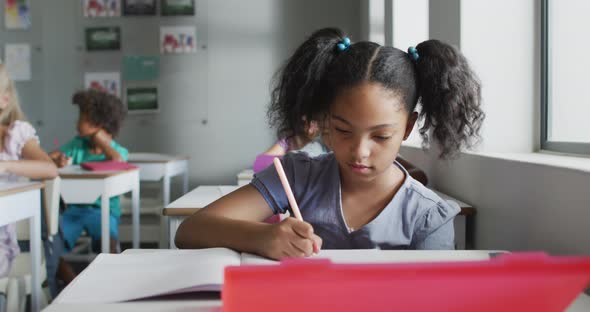 Video of focused biracial girl sitting at desk in classsroom