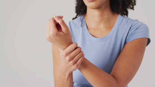 Video of biracial woman touching her wrist on white background