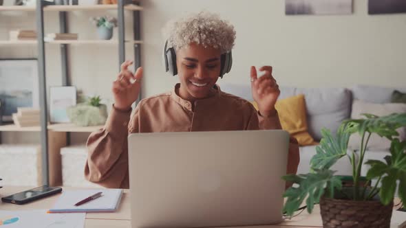 Smiling African Woman Putting on Wireless Headphones Starting Work Day Remotely