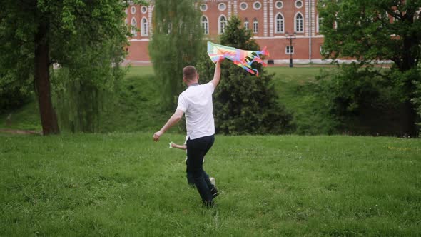 Man Launches a Kite in a Park on a Green Field and a Family Runs After Him