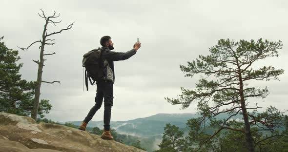 A Man is Standing on Top of a Cliff and Taking Photos of Nature