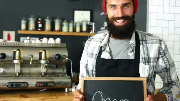 Portrait of waiter standing with open sign board