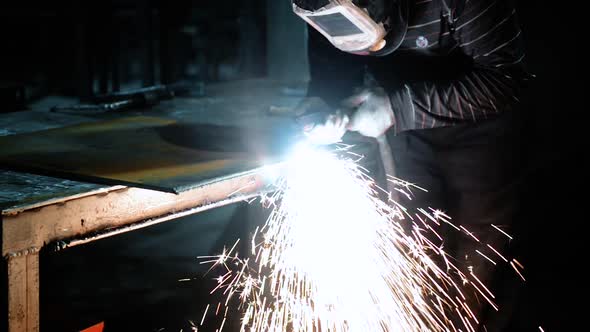 Welder at Work. Worker Welds Metal Parts. Welding Process, Sparks, Flame, Smoke.