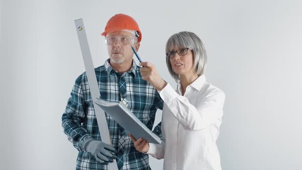 An Elderly Worker in a Helmet and a Female Engineer with a Tablet and a Level in Their Hands Discuss