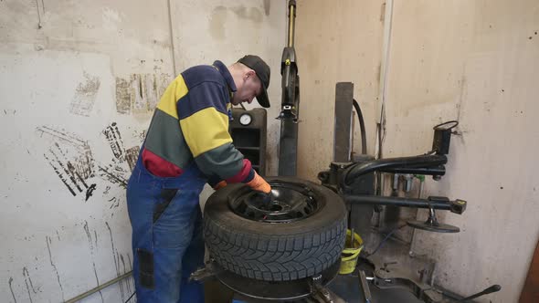 Technician Worker Examines the Tire on Wheel in Garage
