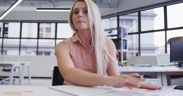 Caucasian businesswoman having video chat going through paperwork in modern office
