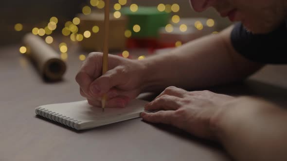 Orbit Shot of Man Writes New Year Goals in Notepad with a Pencil Under Warm Light in the Evening