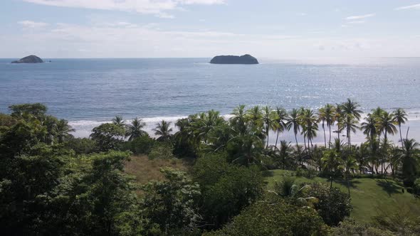 wide aerial drone shot of the jungle and beach merging into the Pacific Ocean with two rocky islands