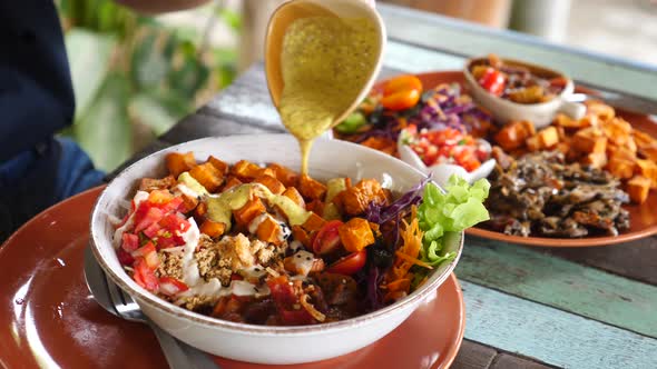 Closeup Of Pouring Sauce On Vegan Bowl With Sweet Potato And Vegetables. Healthy Food.