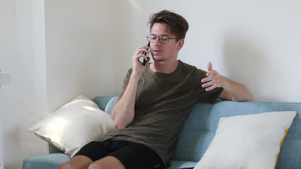 Young Modern Guy Communicates on the Phone While Sitting in the Room on the Couch