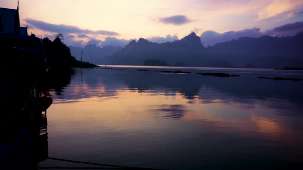 View Over Calm Tranquil Cheow Lan Lake With Morning Sunrise Light And Mountains Being Reflected On L