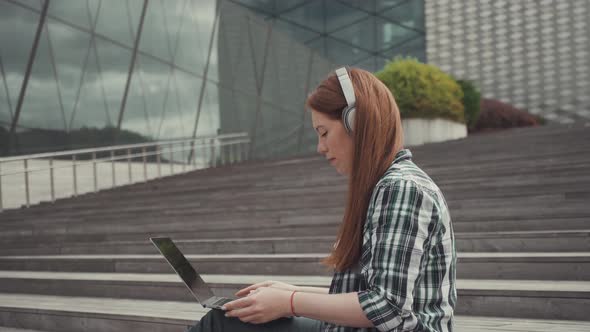 Caucasian Woman Working on Laptop Against the Backdrop of an Office Building