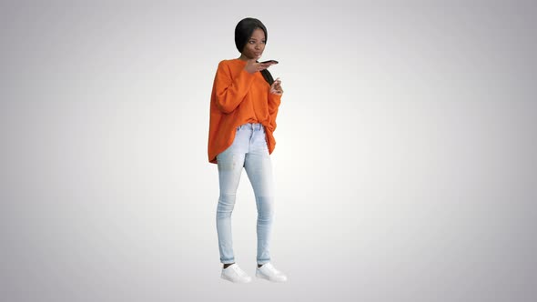 Pretty African American Woman in Bright Jumper Dictating Message Using Her Phone on Gradient