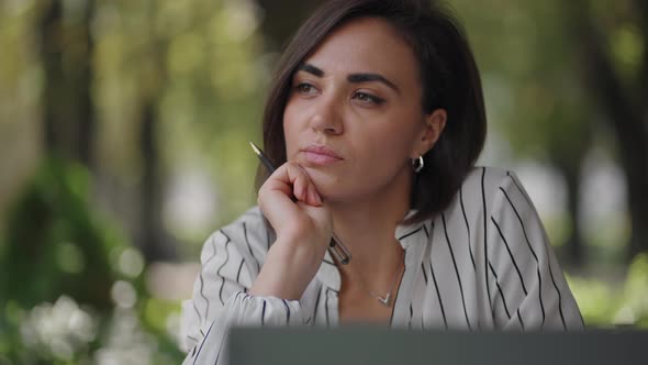 Pensive Woman Brunette Arabic Hispanic Ethnic Group Sits at a Table in a Summer Cafe with a Laptop