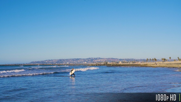 Surfer Guy with Surfboard Walking out of Water Towards Beach