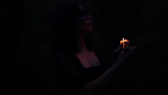 Witch with burning candle in dark woods