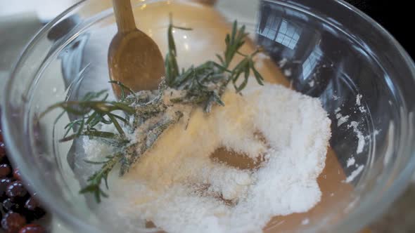 Slow motion wooden spoon stirring and mixing fresh green rosemary and white sugar in large clear gla