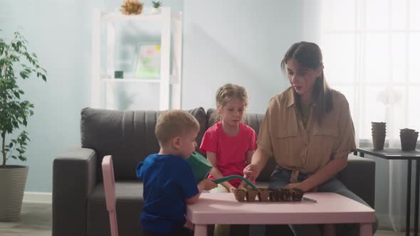 Toddler Boy Waters Seeds in Tray with Mother and Sister