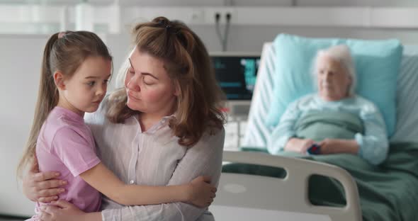 Upset Young Woman and Little Girl Hugging Each Other Visiting Dying Grandmother in Hospital