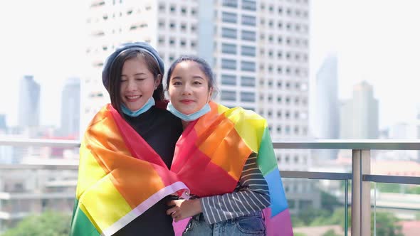 Happy loving homosexual lesbian LGBT couple with rainbow flag at city streets