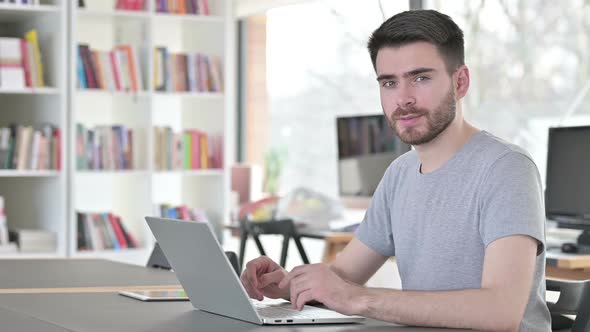 Young Man with Laptop Looking at Camera in Office