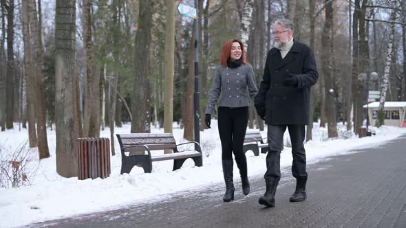 A gray-haired man and his wife are walking in the park on a winter day