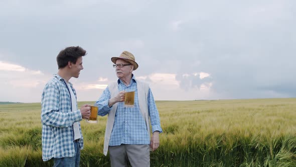 Senior Farmer with Son Clinking Pints of Beer and Having Talk in Barley Field