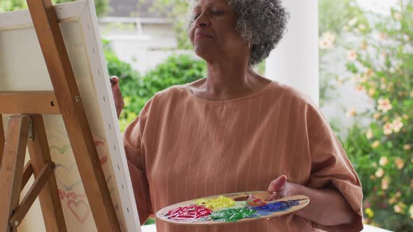 Senior african american woman painting while standing on the porch of the house