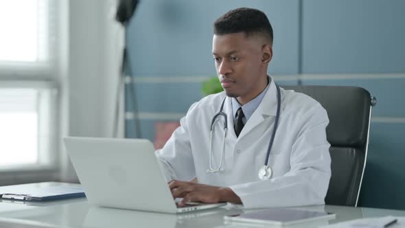 African Doctor Looking at Camera while using Laptop in Office