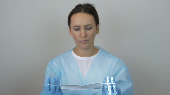Woman in doctor uniform and surgical blue gloves putting on protection mask preparing for surgery