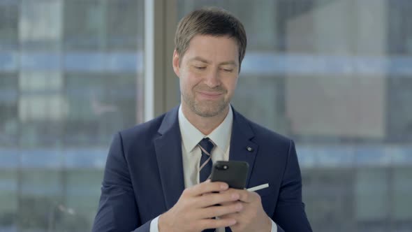 Businessman Scrolling Smartphone at Work