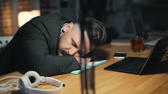 Portrait of Tired Handsome Man Sleeping on Desk in Dark Office Late at Night
