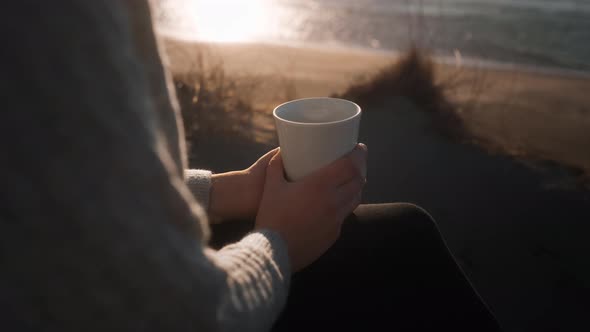 Woman Holding Coffee Cup On Sunlit Beach
