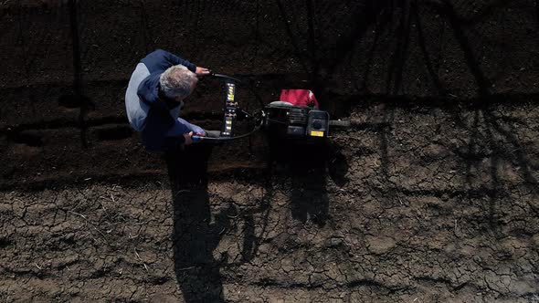 Aerial Drone View Man Farmer Working in the Garden Plows with Garden Tiller