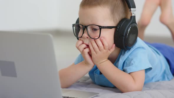 Child in Headphones Looking Into Opened Laptop Screen Listening Talking Online