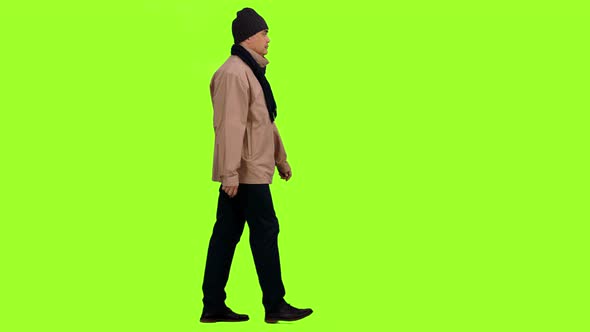A Male in Brown Jacket with Scarf and Hat Walks on Green Background