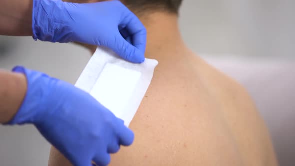 Doctor Hands Applying Adhesive Bandage on Scratched Shoulder of Male Patient