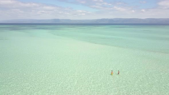 Aerial View of Tourist Couple Walking in the Crystal Clear Shallow Ocean Water.