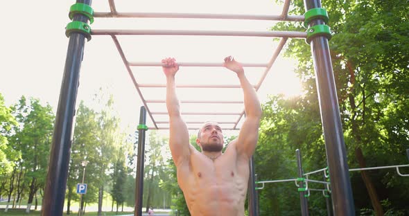 Athletic Man Shirtless Swinging Exercising on Monkey Bar at Sports Ground in Park