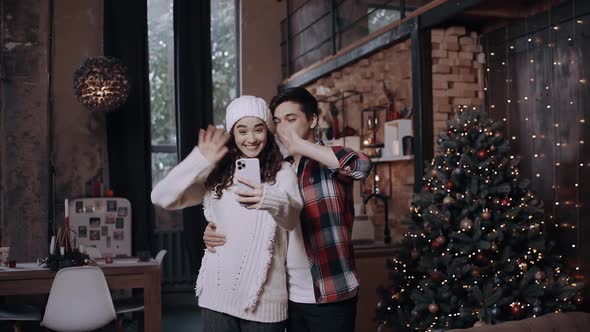Young Cherry Couple Using Smart Phone Talking To Family Congratulates Merry Christmas