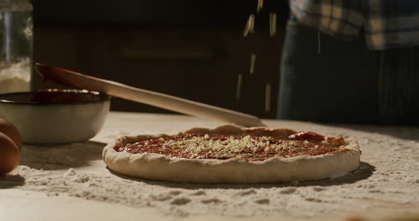 Close Up Shot of Chef Putting Shredded Cheese on Pizza Dough with Tomato Sauce