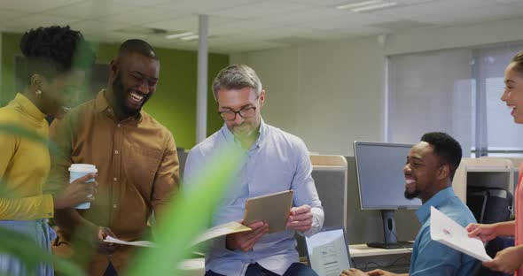 Happy diverse male and female business colleagues using tablet and talking in office