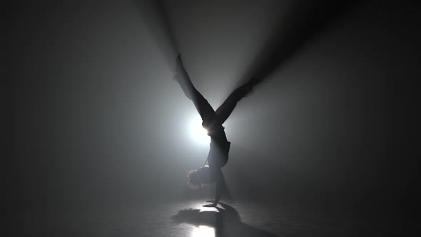 Athletic Girl Practicing Capoeira in Darkness Against Spotlight in Studio