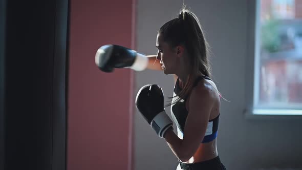 Slow Motion of a Girl Preparing for a Boxing Competition and Trains Punches on a Punching Bag in a