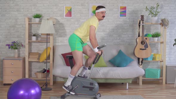 Funny Active Athlete From the 80s with a Mustache Engaged at Home on a Stationary Bike Slow Mo