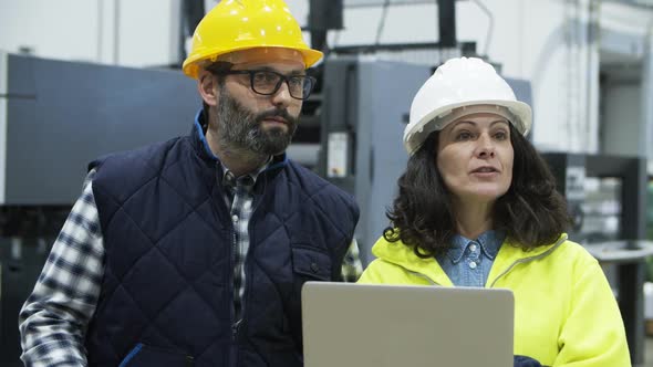 Focused Engineers Discussing Work While Standing with Laptop