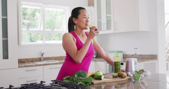 Relaxed asian woman drinking smoothie in kitchen