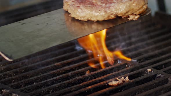 Slow motion of beef hamburger on a grill in close up with flames and smoke