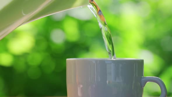 Pours Hot Water Into a Cup on a Table in a Garden Landscape