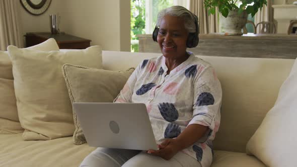 African american senior woman wearing headphones smiling while having a video call on laptop at home